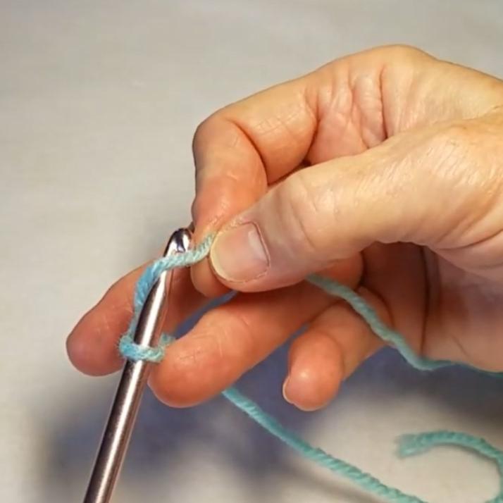 screenshot with cheryl having a crochet hook in her wrist brace and using one hand to crochet